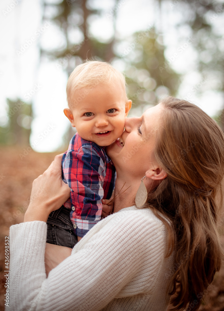 Adorable little boy smiling at the camera while his mother is hugging ...