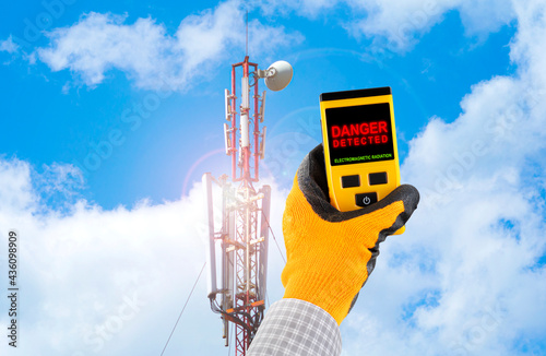 Measuring electromagnetic radiation from a cell tower. The device indicates hazardous radiation with text Danger. Influence of the electromagnetic field on humans concept.