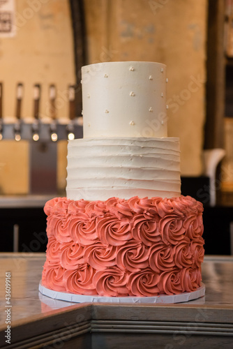 Layered wedding cake with salmon colored flower design and white icing. Side view with bar backdrop