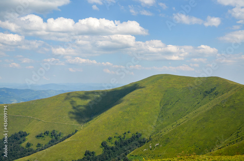 Blue sky with fluffy clouds over the Borzhava mountain ridge with grassy hillside. Gorgeous nature of Carpathian Mountains