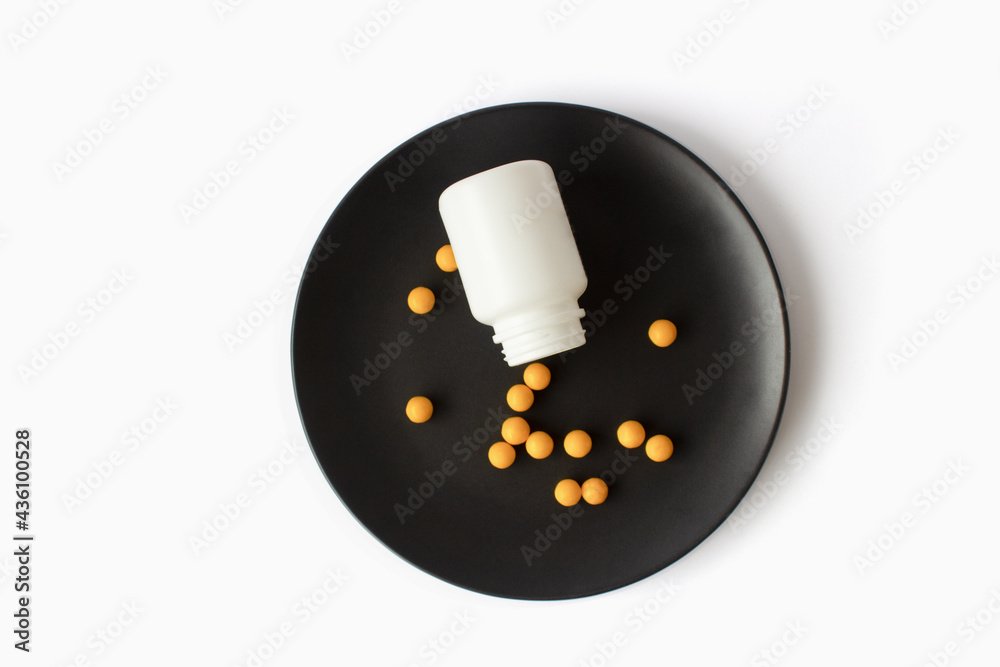 Yellow vitamins pills on a black plate on a white isolated background. Breakfast pills. Yellow vitamins pills on a black plate on a white isolated background. Breakfast pills.