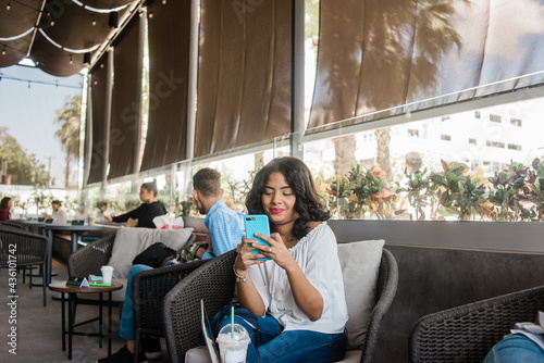 Chica chapando con su celular sentada mientas se toma una bebida fría.