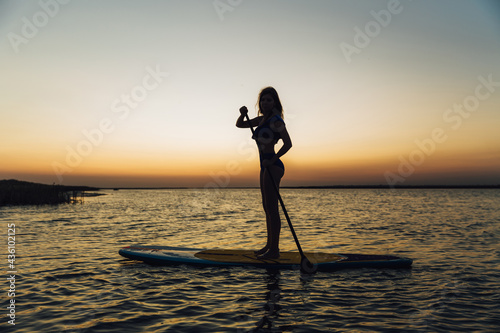 Photography Young beautiful girl in a bikini is resting on a surfboard at sunset