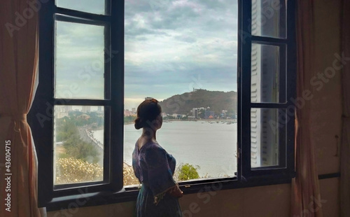 A girl stands and looks out the window at the coastline and the sea. View of Bạch Dinh (Villa Blanche). Vung Tau. Vietnam. South-East Asia Free Download A girl stands and looks out the window at the coastline and the sea. View of Bạch Dinh (Villa Blanche). Vung Tau. Vietnam. South-East Asia - GFXLoad