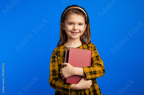 Little schoolgirl in casual dress holding books against blue background