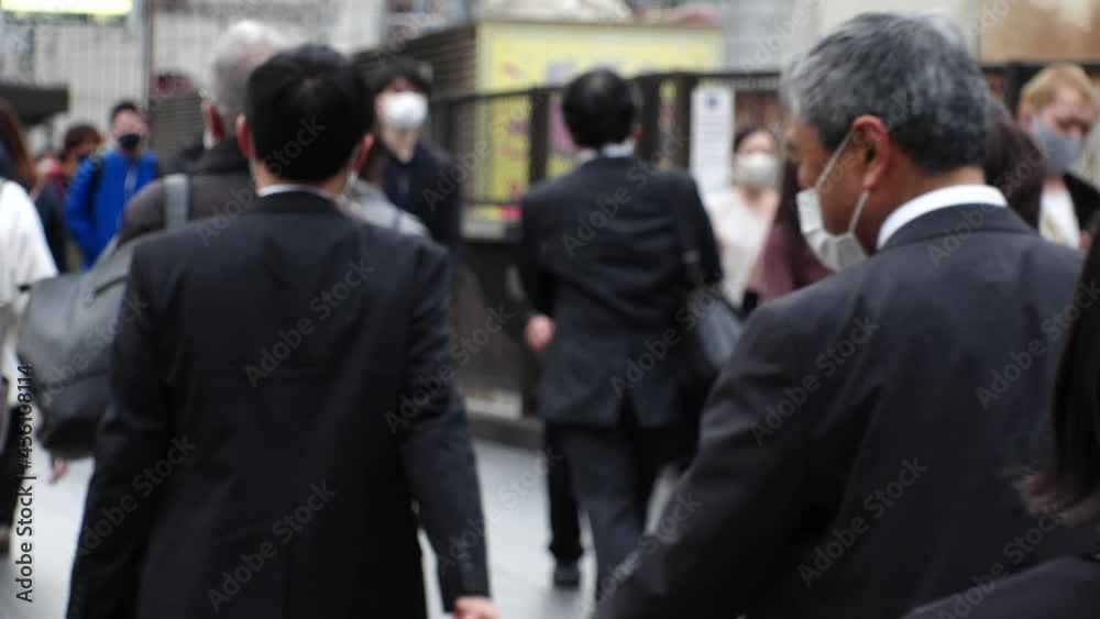 OSAKA, JAPAN - APRIL 2021 : Back shot and unidentified crowd of people wearing surgical masks to protect from Coronavirus (COVID-19) at the street. Slow motion shot. In front focus. OSAKA, JAPAN - APRIL 2021 : Back shot and unidentified crowd of people wearing surgical masks to protect from Coronavirus (COVID-19) at the street. Slow motion shot. In front focus.