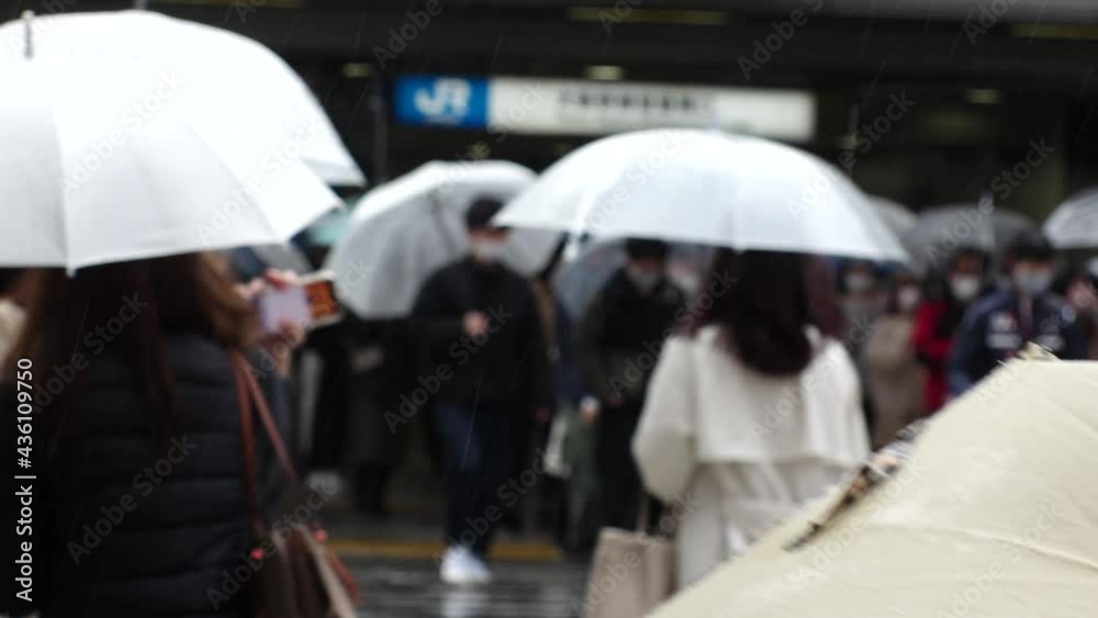 OSAKA, JAPAN - APRIL 2021 : Unidentified crowd of people wearing surgical masks to protect from Coronavirus (COVID-19) at the street. Slow motion shot in rain. In front focus.