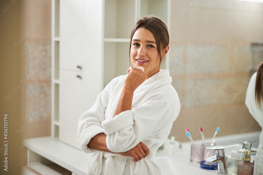Charming elegant female in plush robe holding hand under the chin in bathroom Charming elegant female in plush robe holding hand under the chin in bathroom