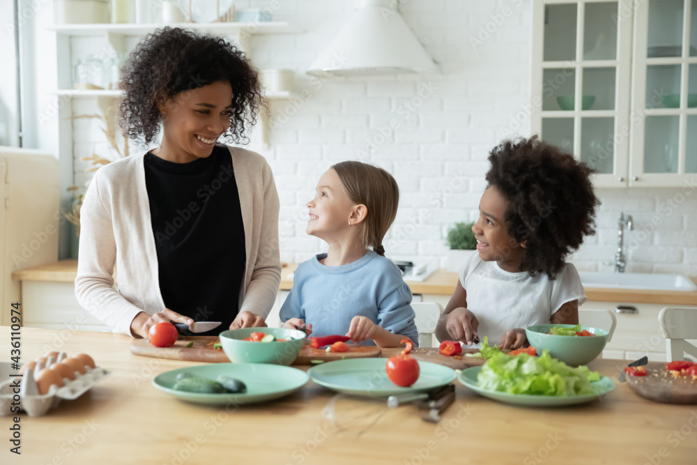 Happy caring young African American mom have fun cook healthy delicious salad with diverse multiracial daughters. Loving smiling biracial mother prepare food with multiethnic kids. Custody concept. Happy caring young African American mom have fun cook healthy delicious salad with diverse multiracial daughters. Loving smiling biracial mother prepare food with multiethnic kids. Custody concept.