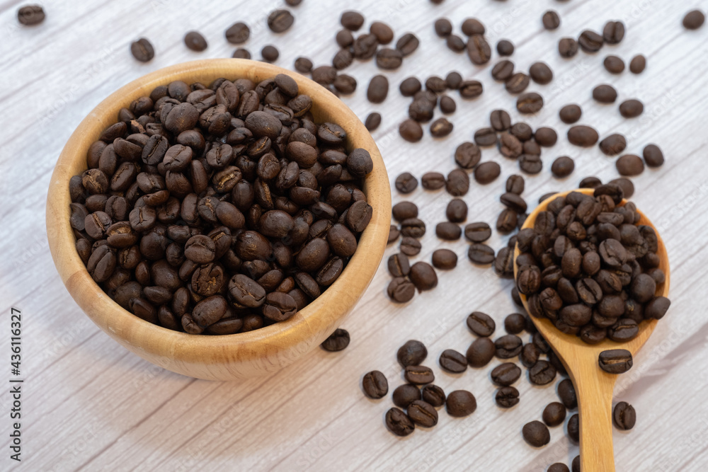 Fototapeta premium Coffee beans in wooden cup and spoon on wooden floor background.