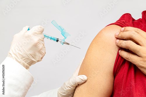 detalhe da mão da enfermeira com luvas segurando a seringa e o paciente, mostrando o braço para aplicação da vacina photo