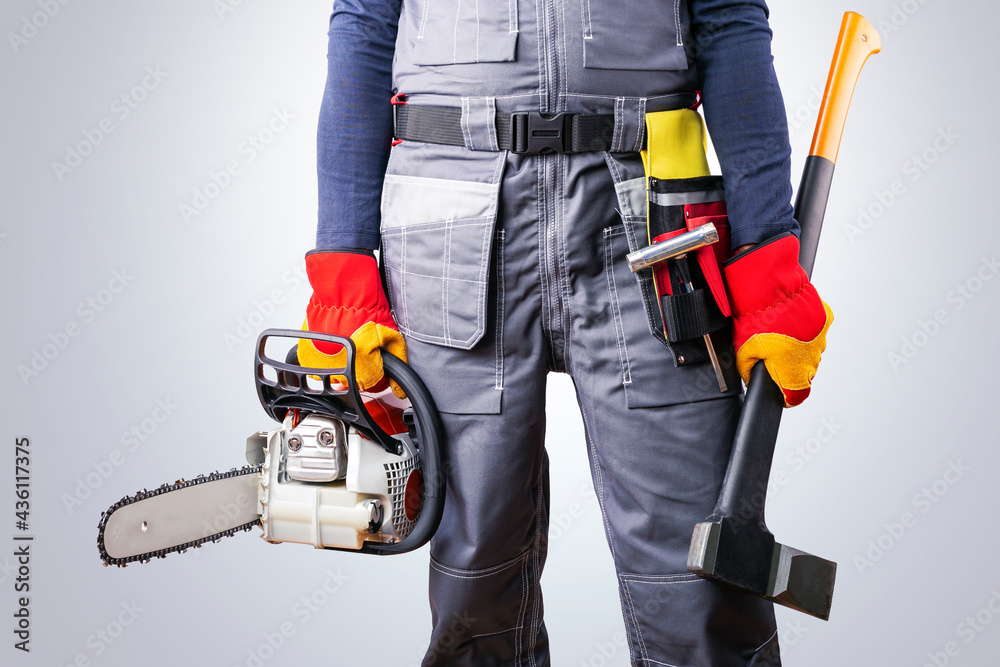 Lumberjack with chainsaw and axe near grey background. Lumberjack with chainsaw and axe near grey background.