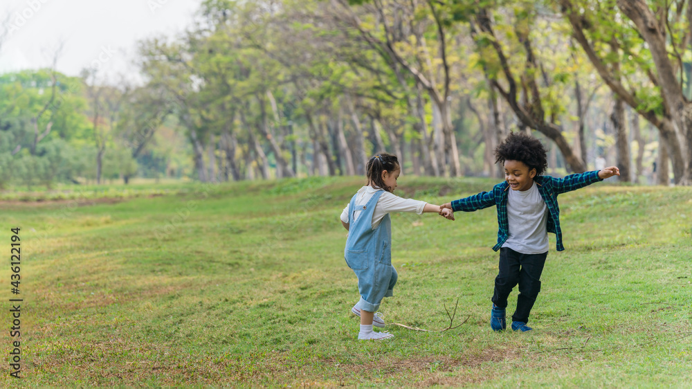 two diverse mixed race children playing and running together in park