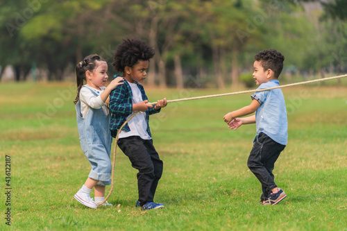 diverse mixed race kids playing pulling rope together in park during summer