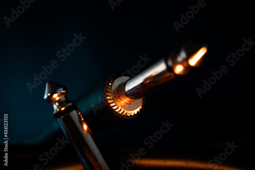 Macro Closeup of Metal Teeth at Base of Quarter Inch Jack Connector Next to Opposite End of Cord on Teal Backdrop with Orange Lighting