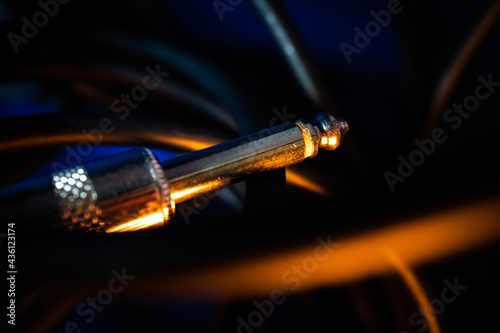 Macro Closeup of Tip on Quarter Inch Instrument Cable Connector Tangled in Cord on Blue Background with Orange Lighting