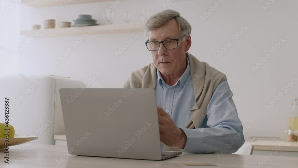 Online shopping via internet. Modern senior man using credit card and laptop for internet purchasing, sitting at kitchen Online shopping via internet. Modern senior man using credit card and laptop for internet purchasing, sitting at kitchen