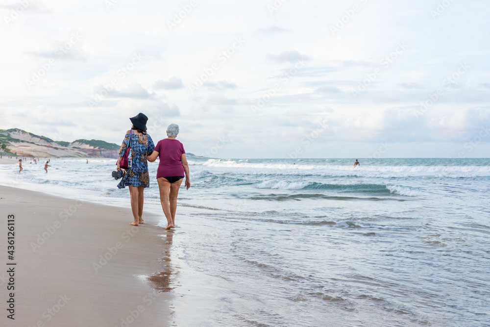 Idosa passeando na praia com apoio da filha