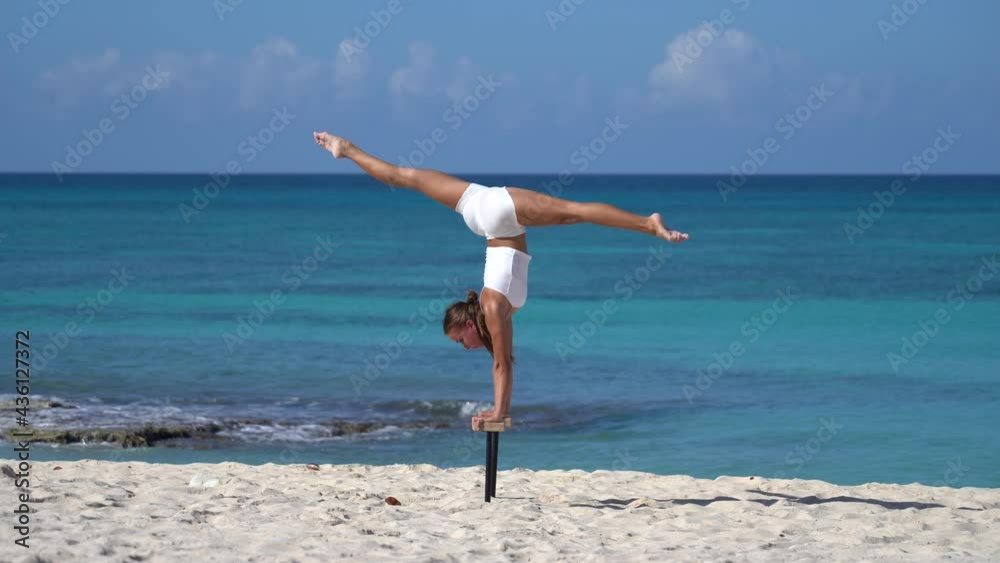 Woman wearing white doing handstand on the beach with sea. Individuality, outstanding and originality. Woman wearing white doing handstand on the beach with sea. Individuality, outstanding and originality.