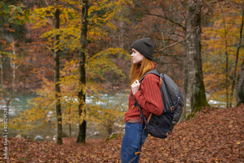 woman with backpack walking in the autumn park near the river in nature side view