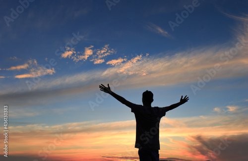 Man with arms raised thanking and praying with the sky after sunset in the background.