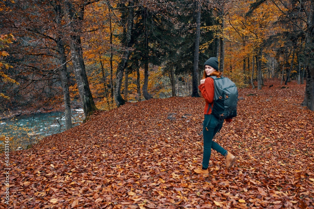 a full-length traveler with a backpack walks in the park with fallen leaves near the river a full-length traveler with a backpack walks in the park with fallen leaves near the river