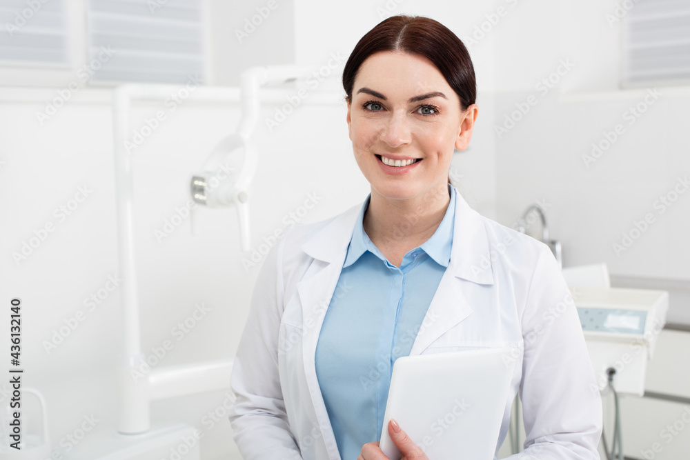 portrait of smiling dentist holding tablet and looking at camera in dental clinic. portrait of smiling dentist holding tablet and looking at camera in dental clinic.