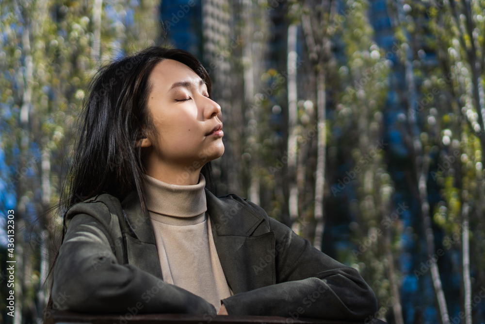 portrait of a young multiracial Asian American business woman with her eyes closed in a park. portrait of a young multiracial Asian American business woman with her eyes closed in a park.