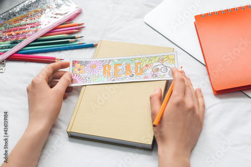 Woman coloring bookmark on bed