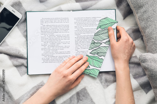 Woman with cute bookmark and book on bed