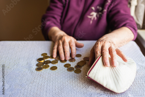 Old woman sitting miserably at home and counting remaining coins from the pension in her wallet after paying the bills. photo