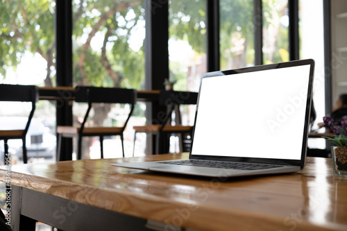 Mock up laptop with white screen on wooden desk in modern coffee shop.
