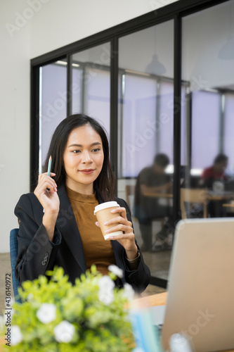 Portrait of confident businesswoman holding coffee cup and having video call with her business partner on laptop computer.