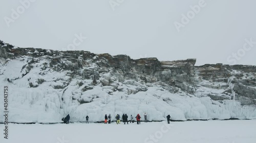 A group of tourists stands on the shore of the frozen Lake Baikal and examines the rocks covered icy splashes - sokui. Slow motion photo