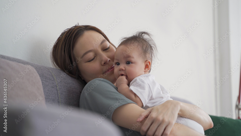 asian woman mother holding happy baby infant playing and kissing on sofa in living room at minimal style home in day time. candid authentic shot life at home. mom play with baby girl by love and care. asian woman mother holding happy baby infant playing and kissing on sofa in living room at minimal style home in day time. candid authentic shot life at home. mom play with baby girl by love and care.