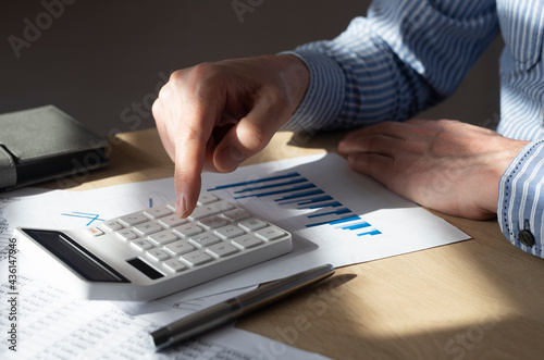 Bild auf Leinwand Male hand at desk with financial document with graph of growing trend, making calculations, preparing report