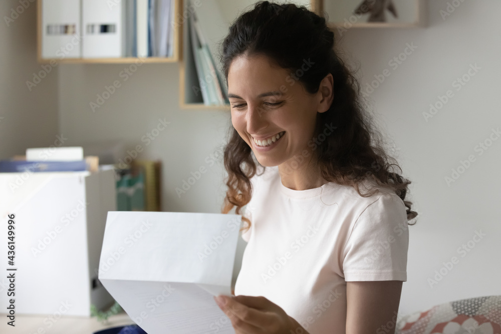 Smiling sincere millennial woman holding paper correspondence, reading letter with good news, feeling excited of getting bank loan approvement notification, taxes refund, university admission notice. Smiling sincere millennial woman holding paper correspondence, reading letter with good news, feeling excited of getting bank loan approvement notification, taxes refund, university admission notice.