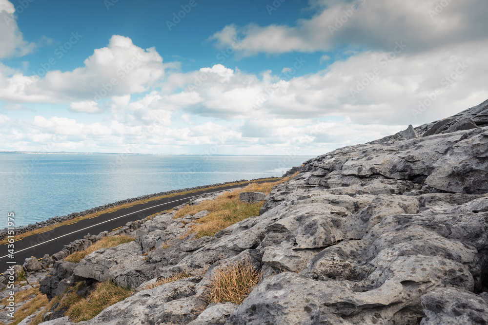 Small asphalt road by the ocean through rough stone terrain, County Clare, Ireland. Blue cloudy sky, Galway bay. Beautiful Irish nature