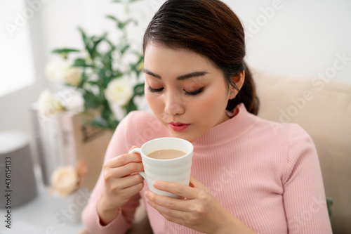 Indoor shot of a smiling asian woman drinking tea.