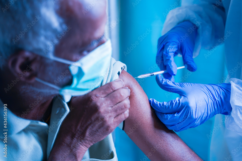 Senior elderly patient with mask getting vaccination or jab at hospital - Doctor in protective Hazmat suit treating Covid patient injecting anti-viral vials at covid care Centre - obrazy, fototapety, plakaty 