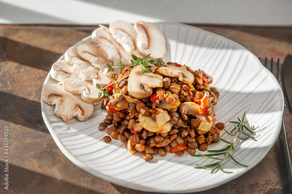 lentils with sliced mushrooms and vegetables. Vegan food - stewed carrots, peppers, onions and lentils with fried mushrooms. Close-up