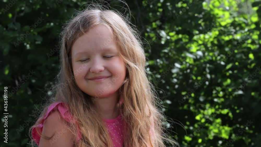 A cute preteen girl with long hair fluttering in the wind. Close-up of a child in the summer on a sunny day outdoors in the garden smiling and looking at the camera. A cute preteen girl with long hair fluttering in the wind. Close-up of a child in the summer on a sunny day outdoors in the garden smiling and looking at the camera.