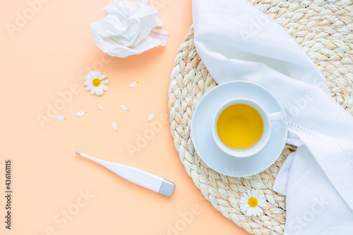 Eine Tasse Kamillenblütentee, ein Fieberthermometer und ein zerknülltes Taschentuch auf einem gelben Tisch. Draufsicht, Kräutermedizin. photo