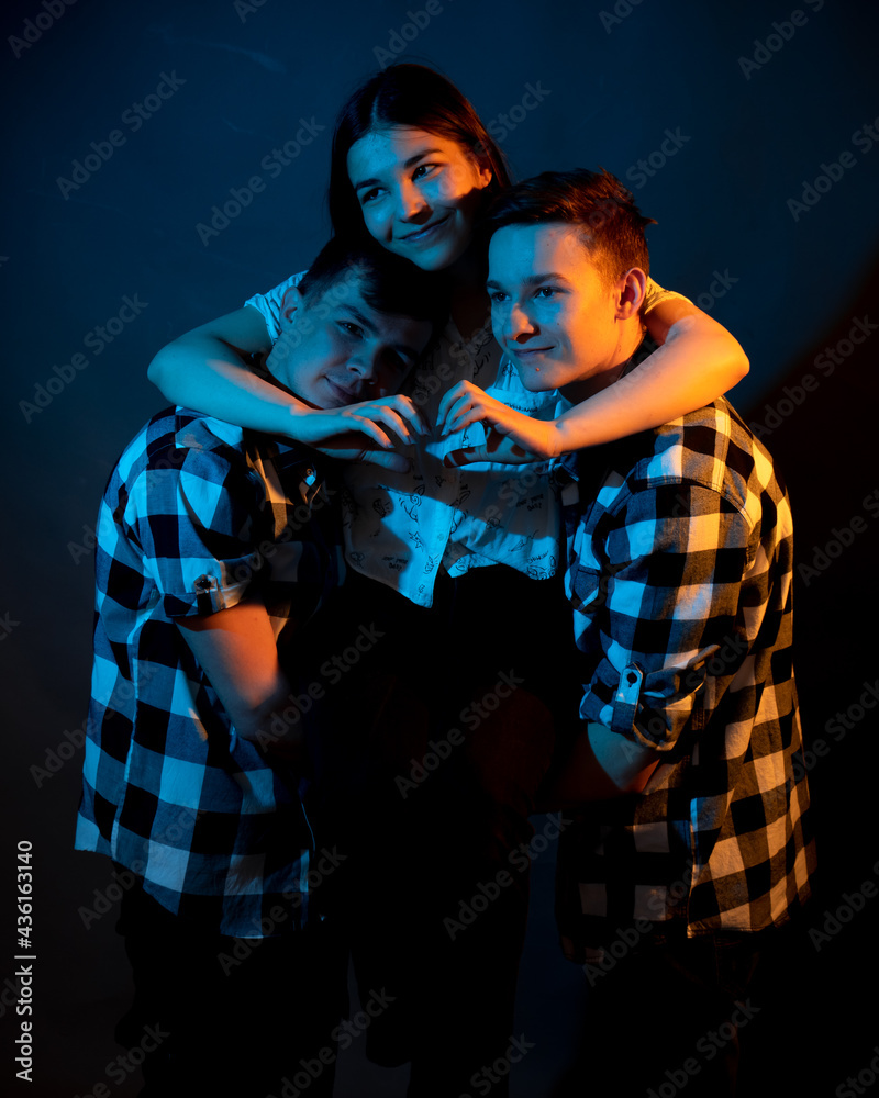 Two guys in a plaid shirt are holding a girl on a dark background in a studio with multicolored light