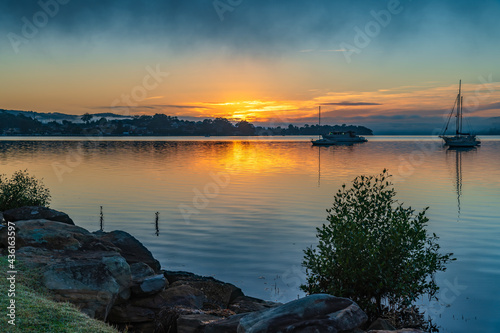 Sunrise waterscape with boats, light cloud and fog