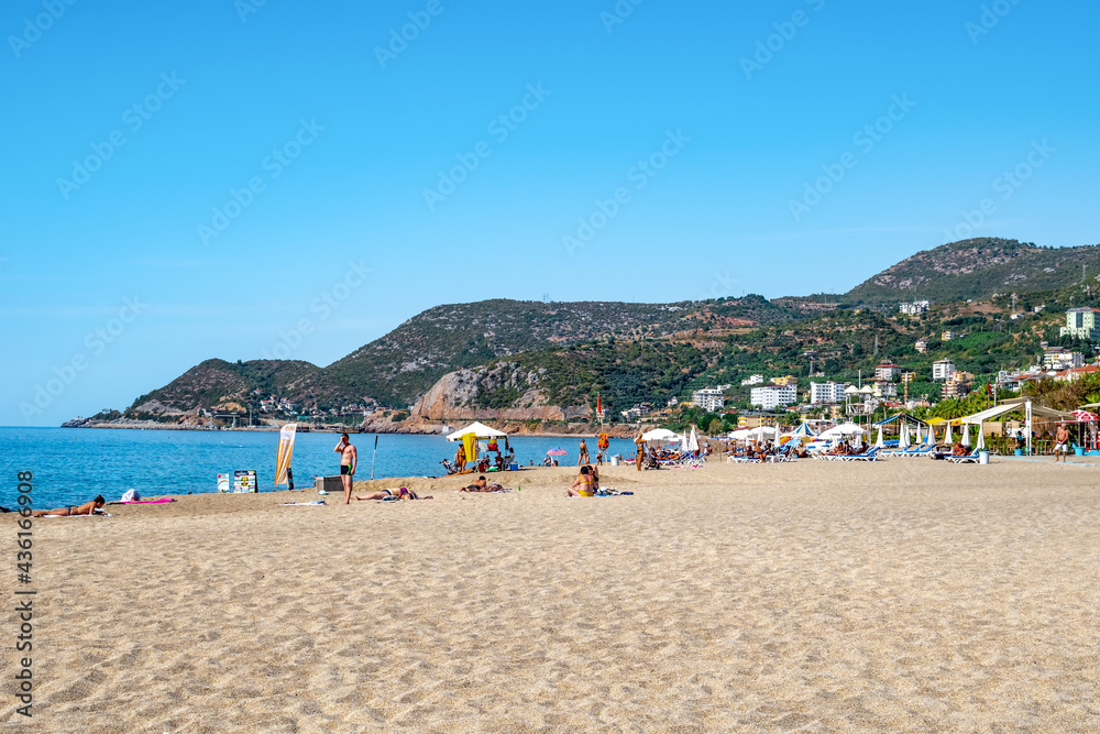Alanya, Turkey - October 23, 2020: Seascape of Cleopatra Beach in Alanya. Beautiful tropical panorama with people having a rest on white sand near blue water on a background of green mountains