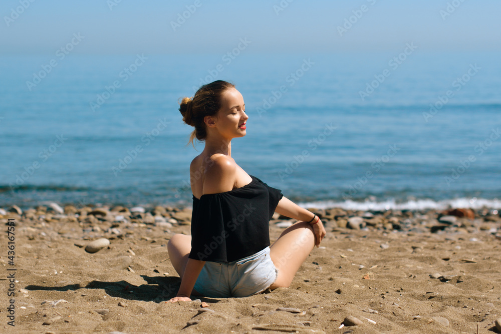 A beautiful girl is engaged in yoga on the beach against the background of the sea. Health and sports. A woman on the ocean shore meditates and relaxes. Summer and travel.