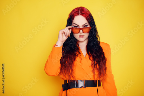 Beautiful girl on a yellow background. A brunette in an orange dress and long hair is posing, smiling, having fun. Woman in sunglasses. Joy and emotion. Red hair roots place for text © MoreThanProd