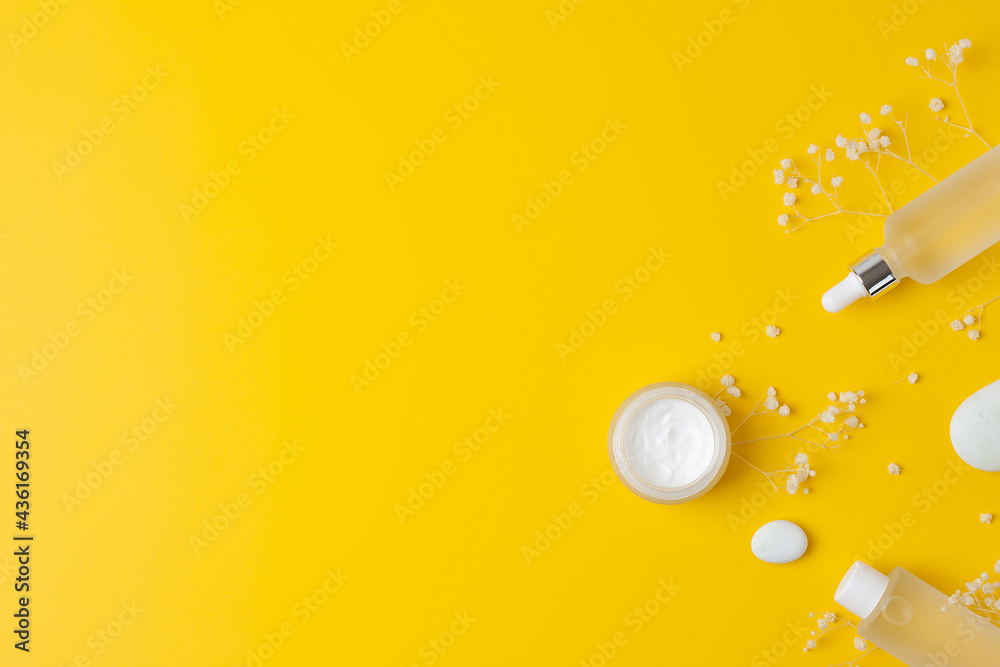 Fototapeta premium Cosmetic skin care products with flowers and stone on yellow background. Flat lay, copy space.