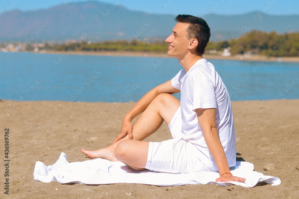 Man enjoys staying on the beach. Man on beach lying in sand looking to side smiling happy. Young male model enjoying summer travel holiday by the ocean.